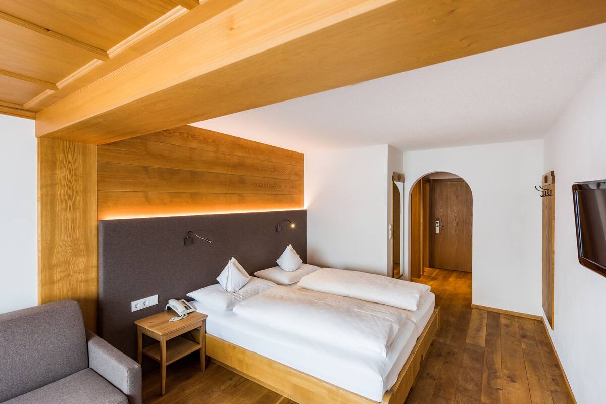 A modern hotel room with a wooden headboard, a bedside table with a phone, and a sofa.