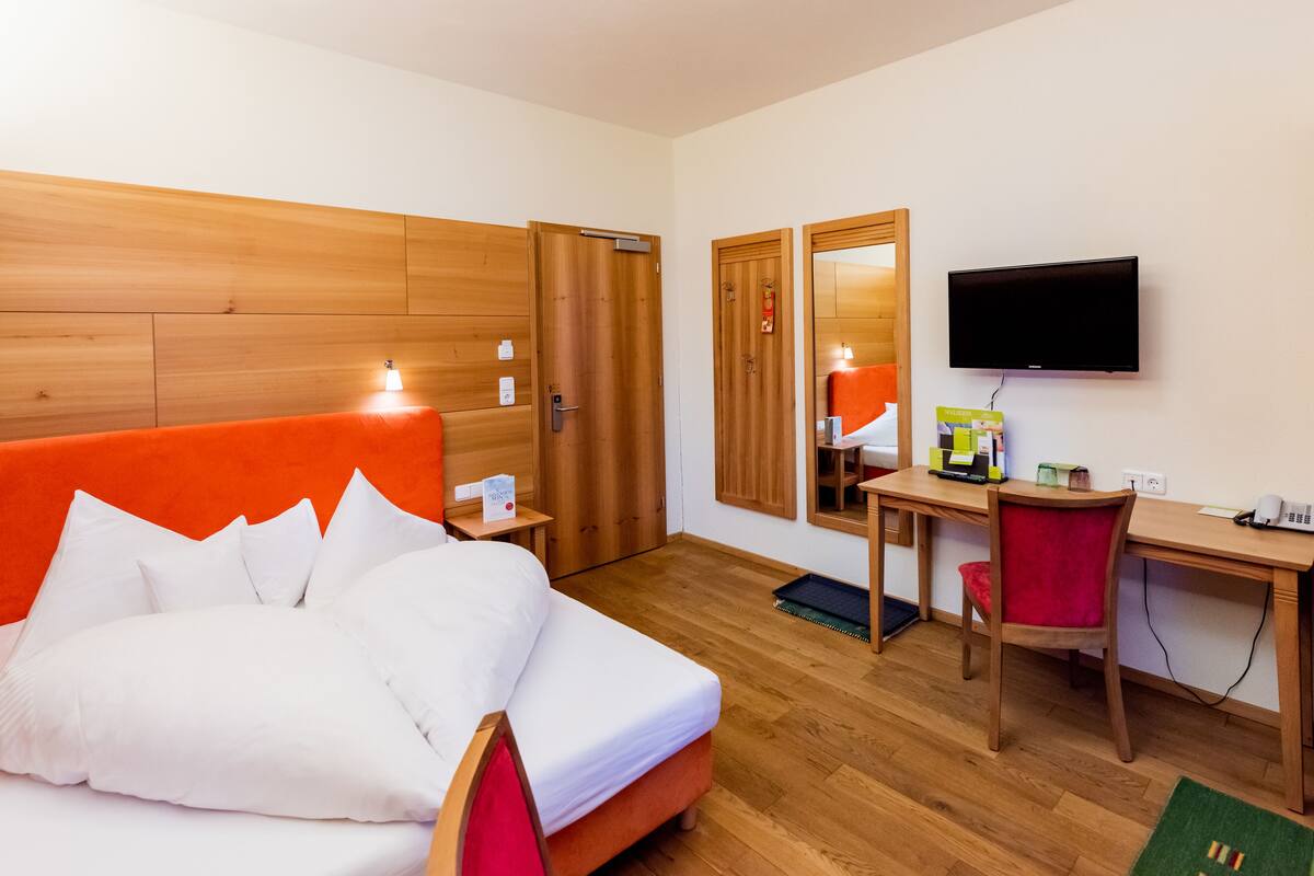 A hotel room with a bed, a desk, a chair, a television, and a mirror.