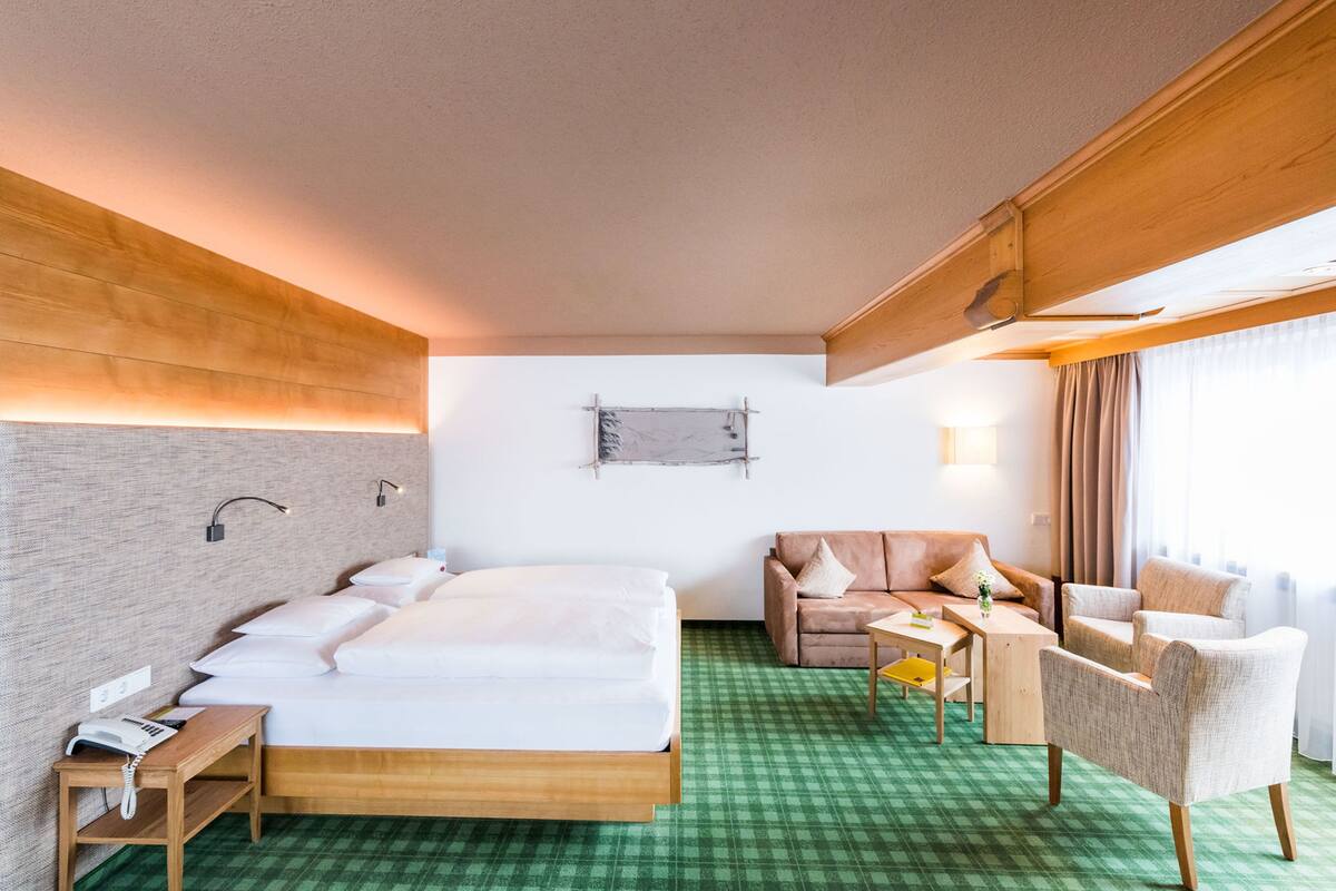 A hotel room with a bed, a sofa, a chair, a small table, and a desk.