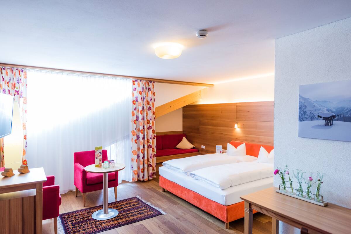 A hotel room with a bed, a desk, a chair, a small table, and a window with curtains.