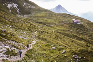 A mountain path with hikers and a small house on a grassy slope. - Hotel Walserberg (Warth)