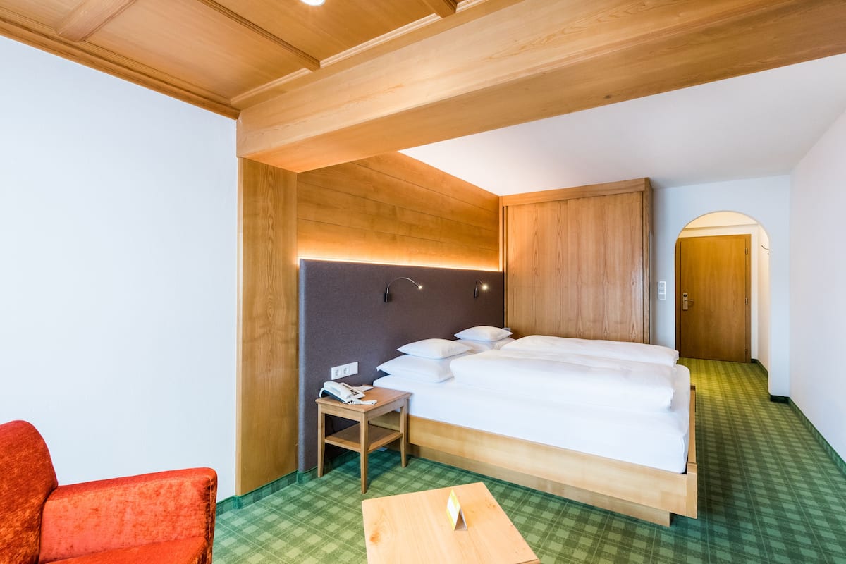 A hotel room with a wooden bed, a small bedside table with a phone, a red chair, and a check-in desk.