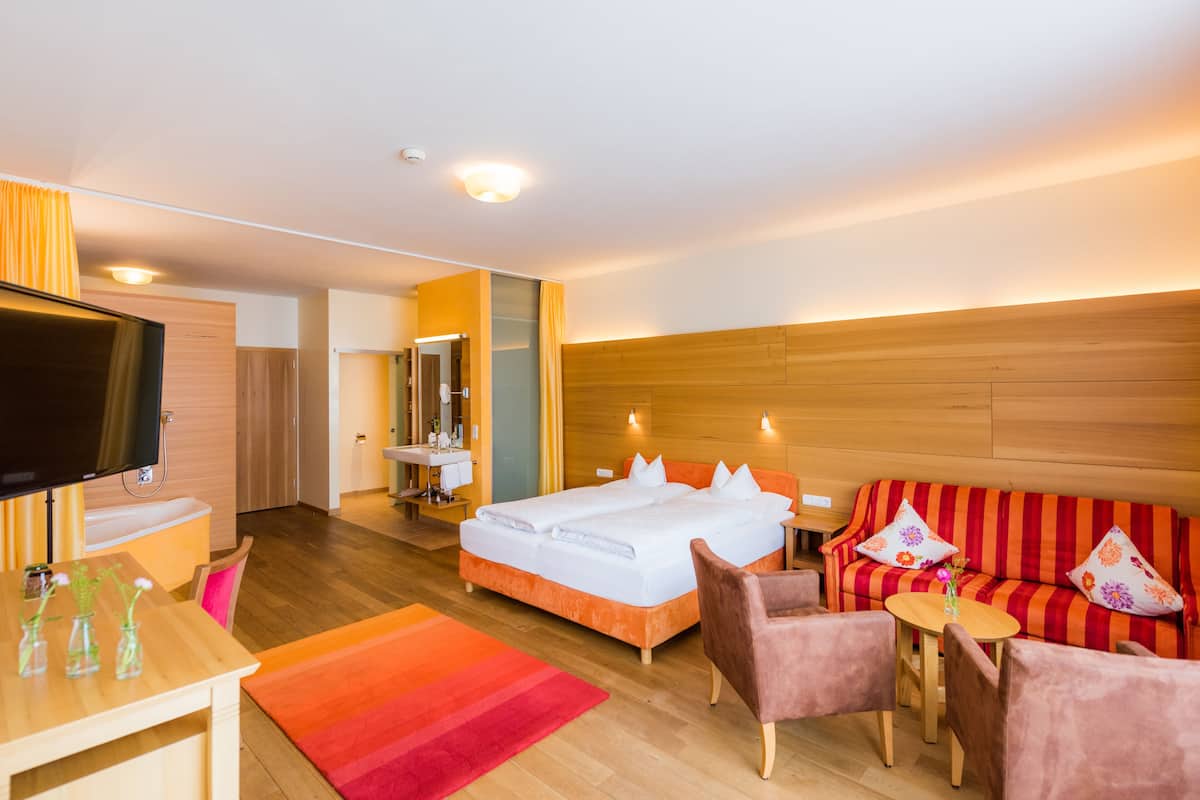 A hotel room with a bed, a sofa, a TV, a desk, and a bathroom.