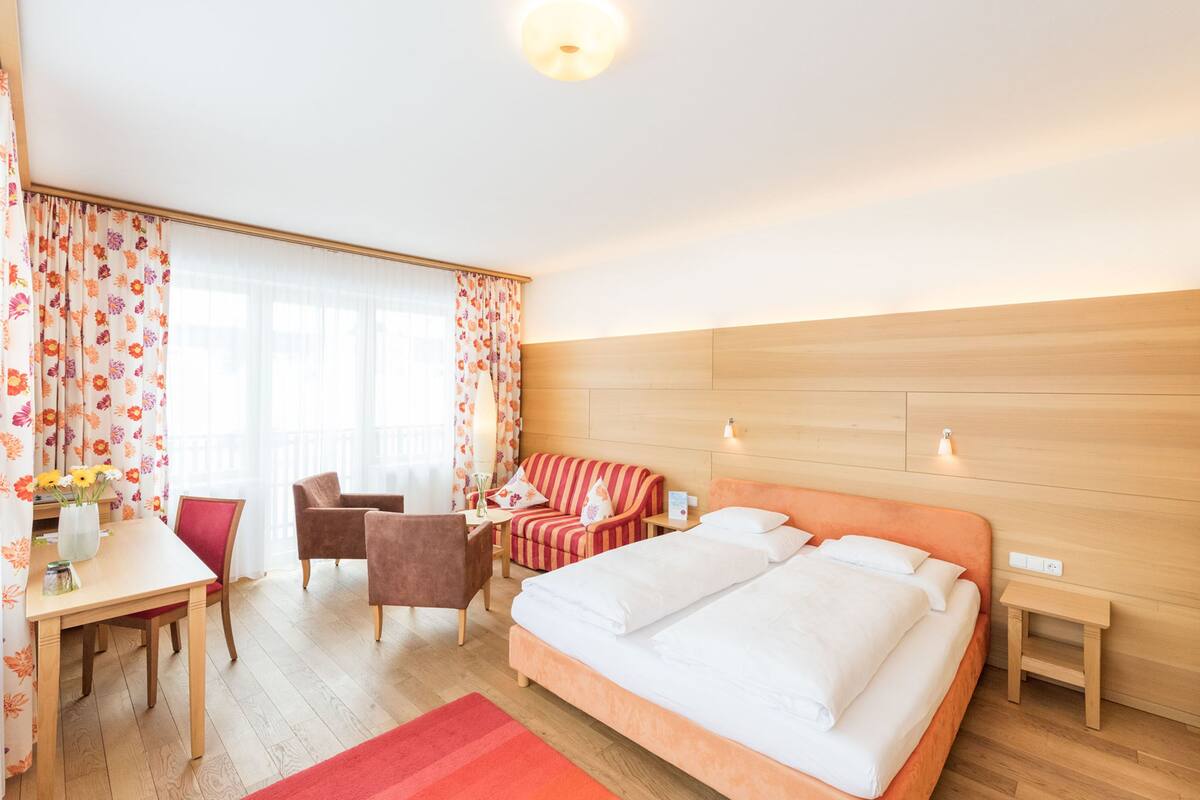 A hotel room with a large bed, a desk, a chair, a sofa, and a small table.