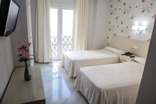 Una habitación de hotel con dos camas, una mesita de noche, un televisor y una ventana con cortinas.