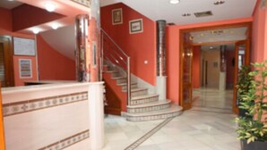 A hotel lobby with a reception desk, a staircase, and a potted plant. - Hostal Chaikana (El Puerto de Santa Maria)