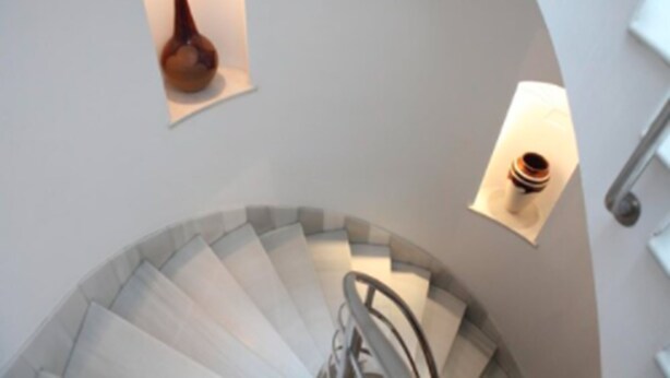 A spiral staircase with a handrail and a light fixture on the wall. - Hostal Chaikana (El Puerto de Santa Maria)