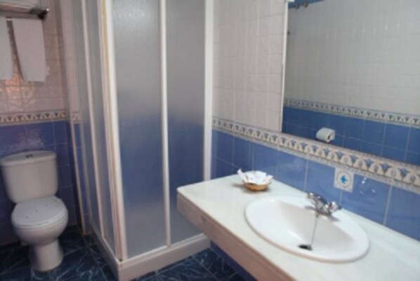 A bathroom with a white toilet, a shower enclosure, and a sink with a mirror.