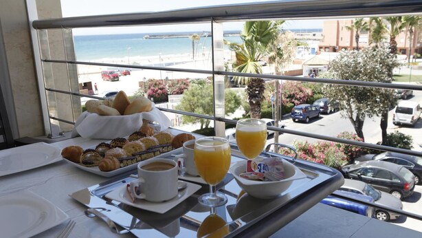 A breakfast tray with pastries, coffee, and orange juice on a balcony overlooking a beach and cityscape. - Adiafa Hotel (Barbate)