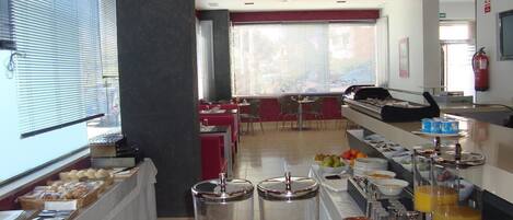 Zona de desayuno tipo bufé con diferentes opciones de comida y un área de estar con mesas y sillas.