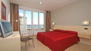 A hotel room with a large bed, a desk with a computer, a chair, a TV, and a view of the sea through large windows. - Adiafa Hotel (Barbate)