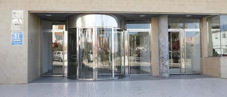 A hotel entrance with a revolving door, a sign for the Adiafa Hotel, and a blue sign indicating a handicap-accessible entrance.