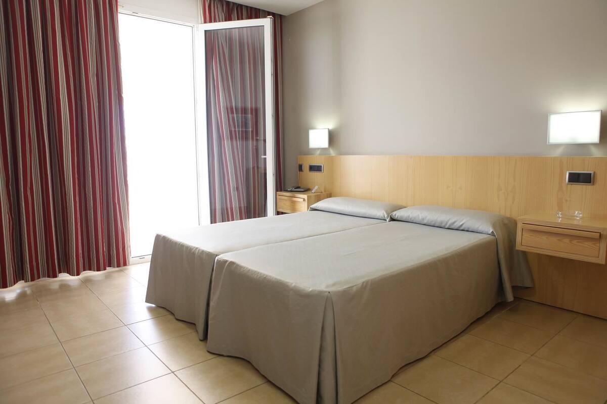 Una cama doble con cabecera de madera, dos mesitas de noche y una ventana con cortinas.