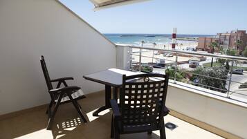Un balcon avec deux chaises et une table, donnant sur une plage et un parking.