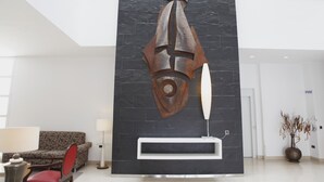 A modern lobby with a large abstract metal sculpture, a white reception desk, a patterned sofa, and a small table with a lamp. - Adiafa Hotel (Barbate)