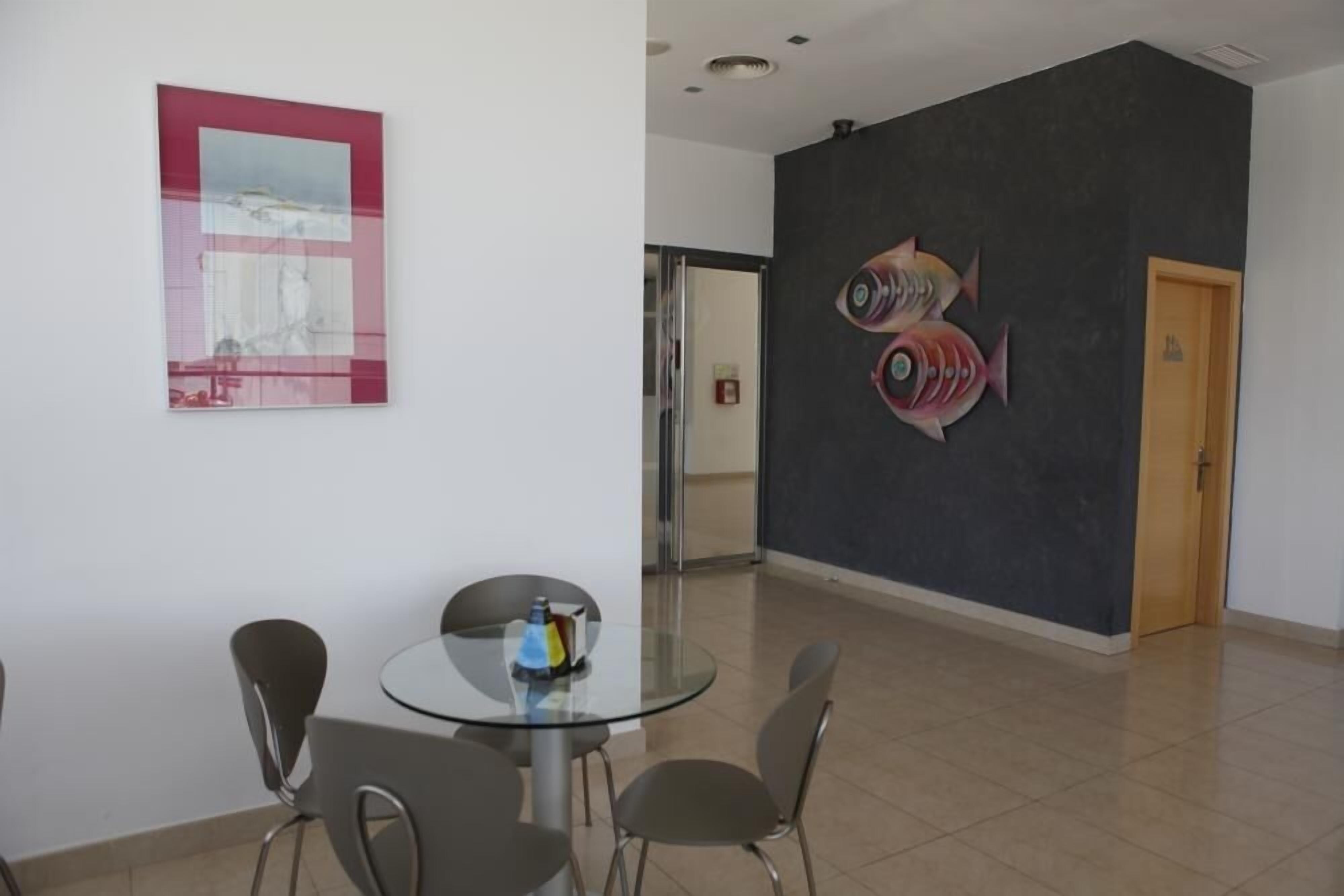 A modern interior with a round glass table, four chairs, a framed artwork, and a fish mural on the wall.
