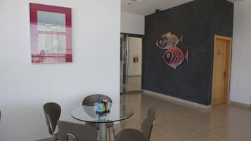Un interior moderno con una mesa redonda de cristal, cuatro sillas, una obra de arte enmarcada y un mural de peces en la pared.