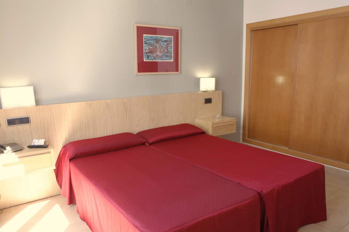 Habitación de hotel con cama, mesitas de noche, lámpara, armario y un cuadro en la pared.