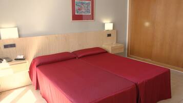 A hotel room with a bed, bedside tables, a nightstand, a lamp, a wardrobe, and a framed picture on the wall.