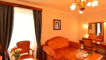 Una habitación de hotel con sofá, una mesa de comedor con un jarrón de flores, alfombra y candelabro.