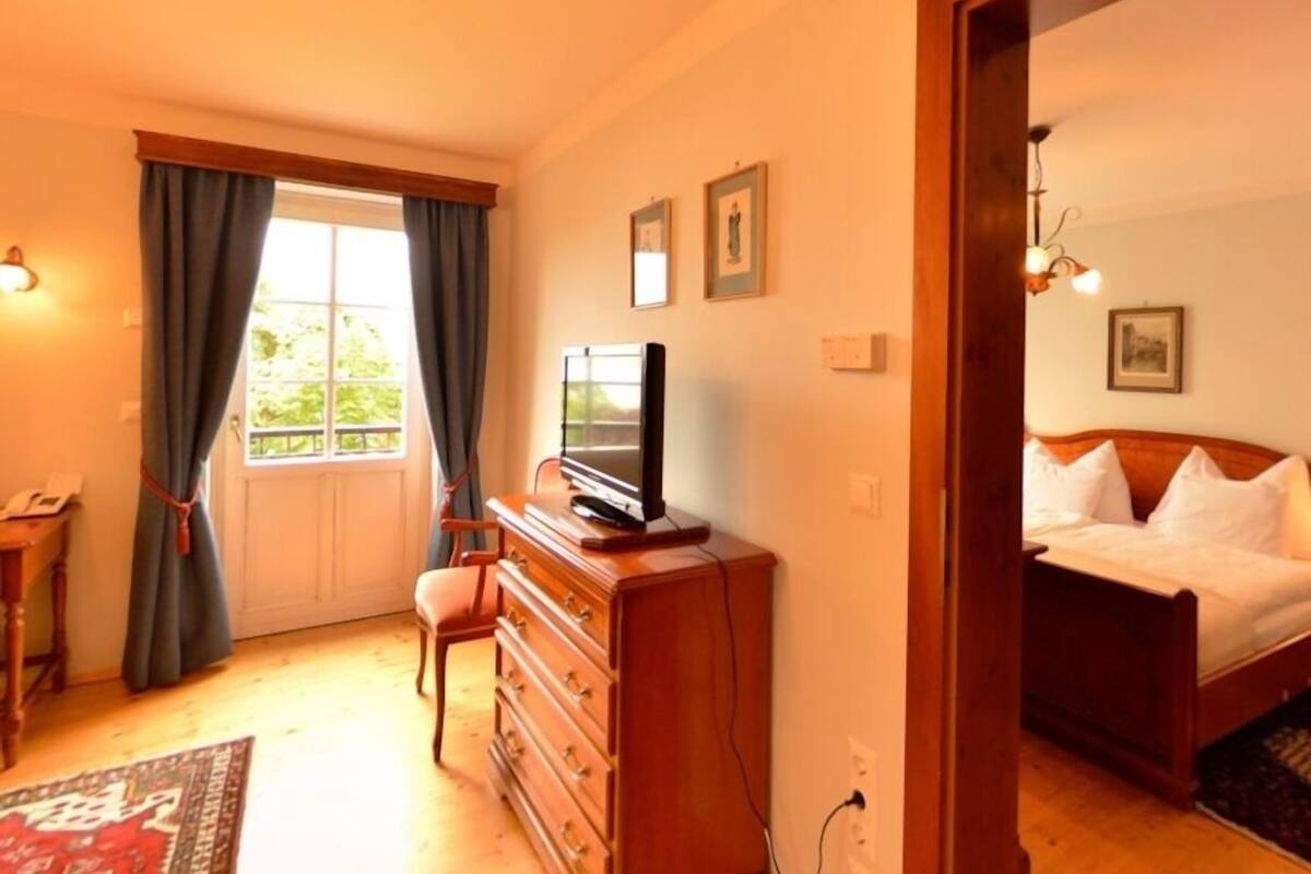 Une chambre à coucher avec un lit, une commode, un téléviseur et une fenêtre avec des rideaux.