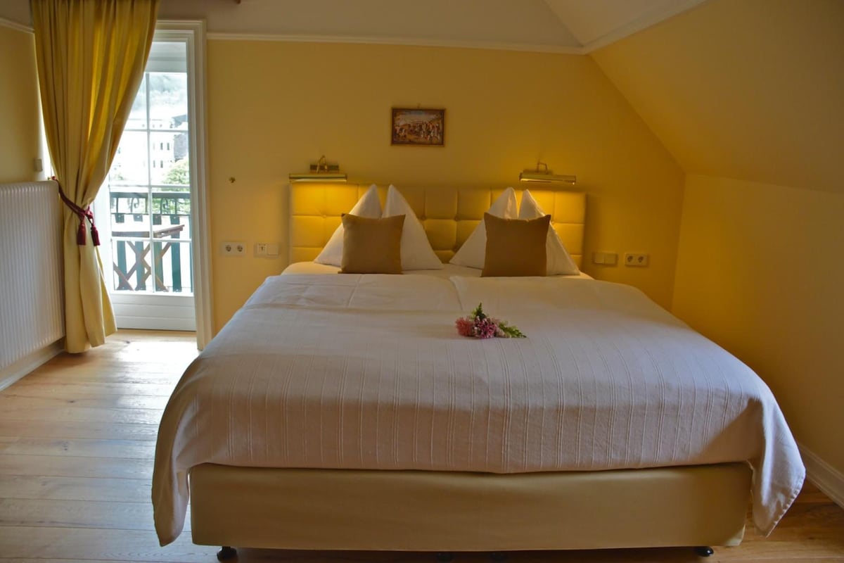 A hotel room with a large bed, a balcony view, and a painting on the wall.