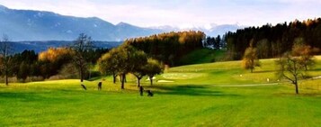 A golf course with a clear view of the surrounding landscape, including trees and distant mountains.