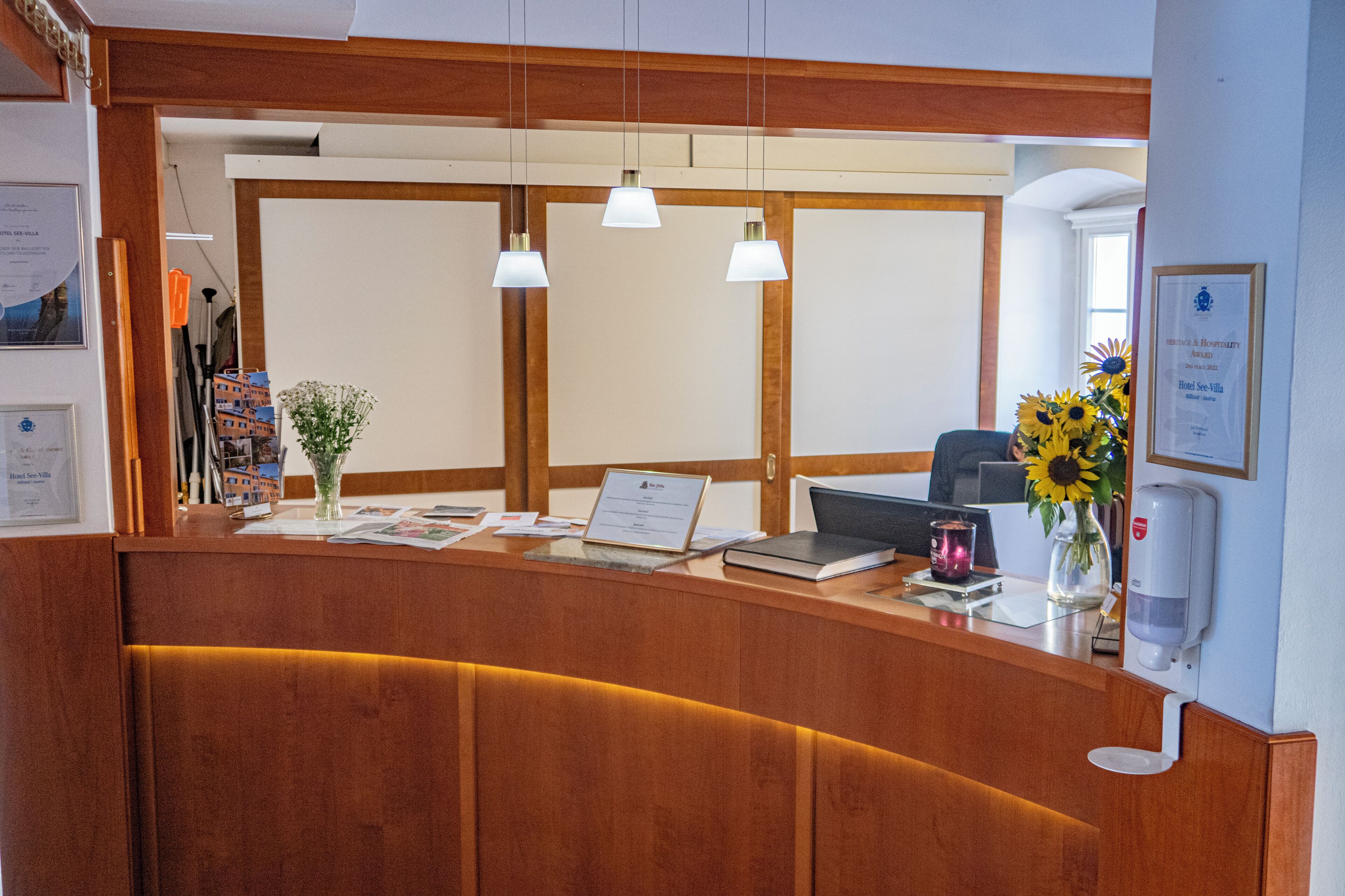 A reception desk with a laptop, a vase with sunflowers, and a framed award on the wall.