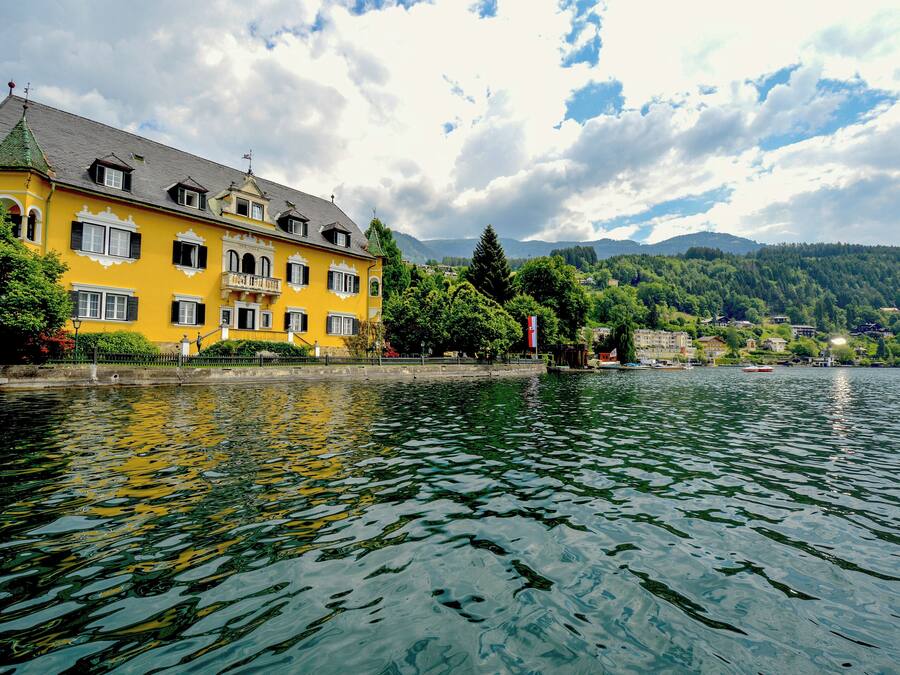 A yellow building with a balcony, located near a body of water with reflections.