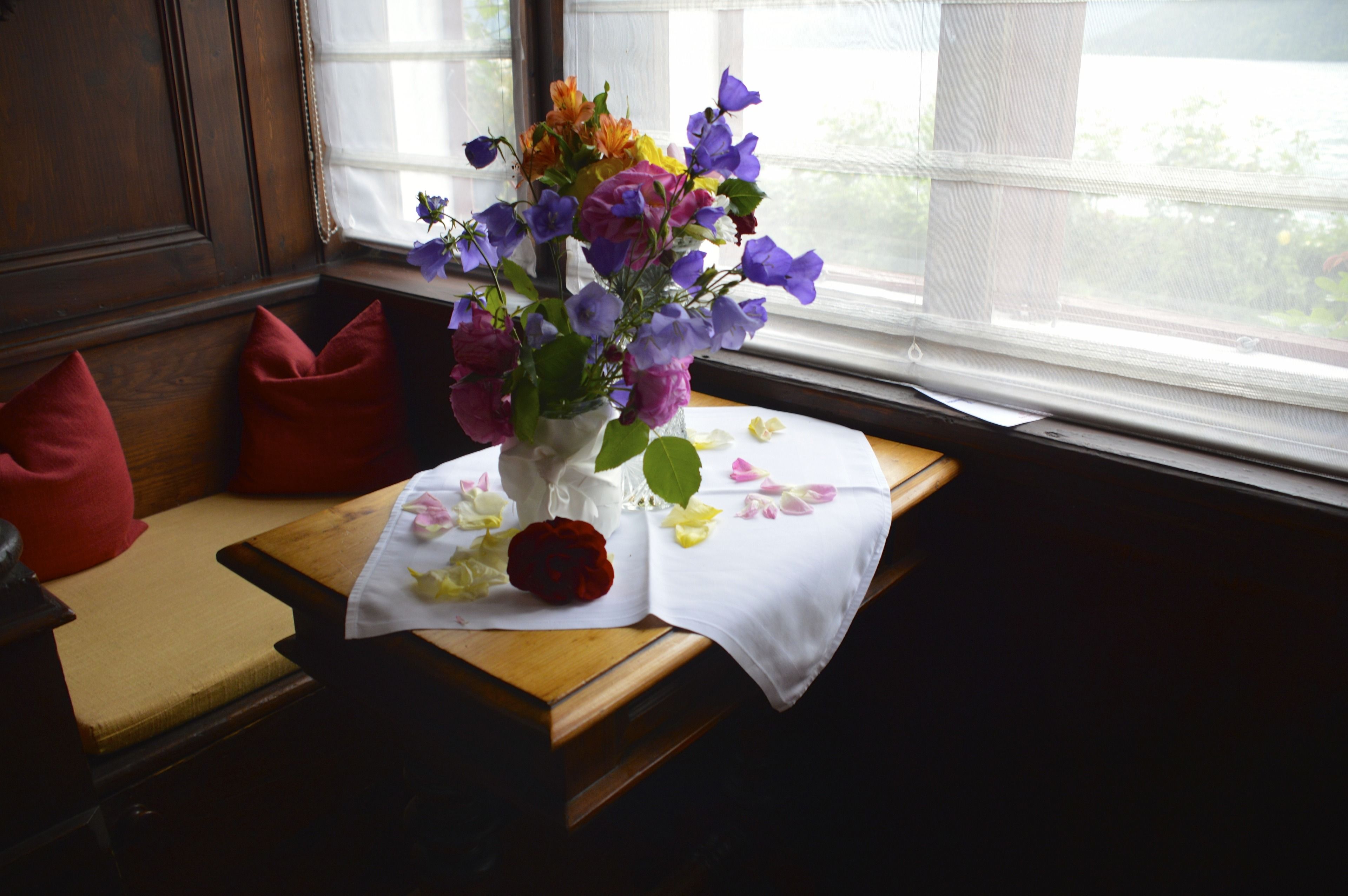 A wooden bench with a white tablecloth, a vase with flowers, and a red rose.