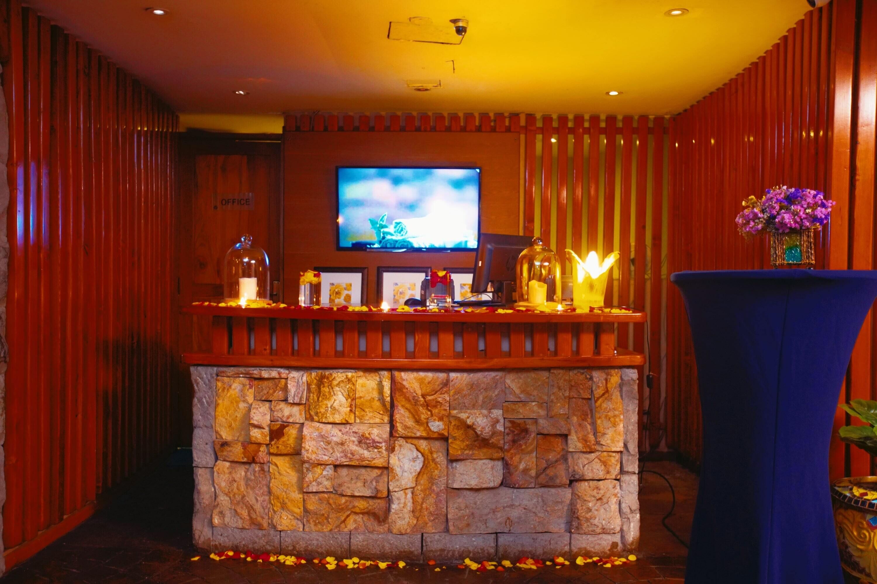 Ein Empfangsbereich mit einer Steintheke, einem an der Wand montierten Fernseher und einer Vase mit Blumen.