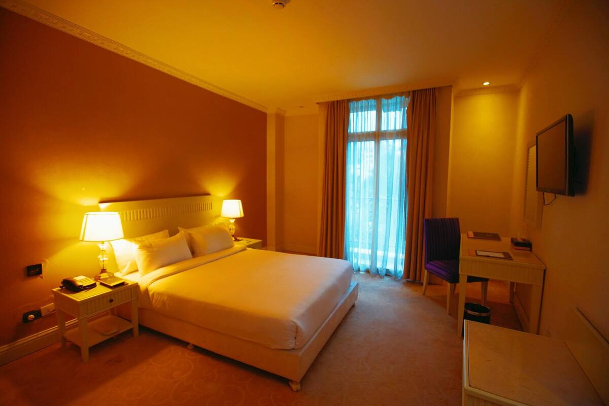 A hotel room with a large bed, bedside lamps, a desk, and a television.