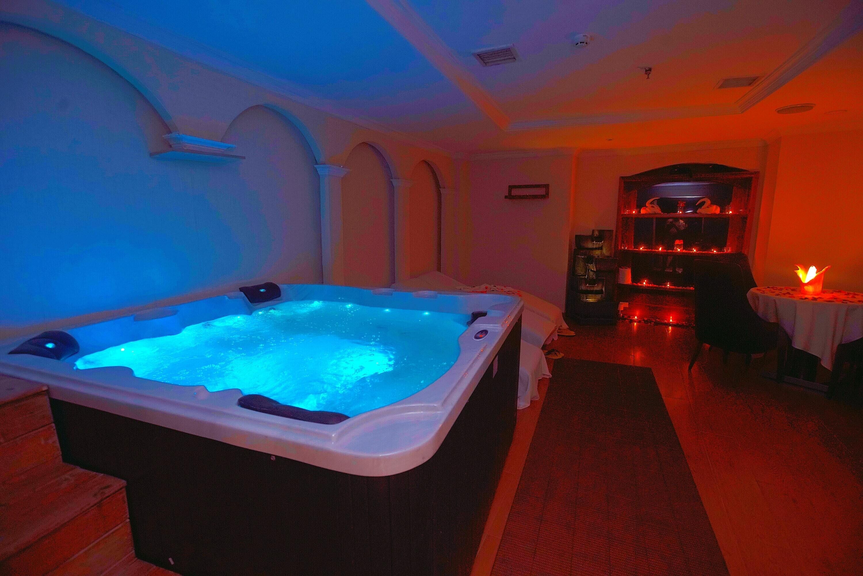 A spa room with a hot tub, wooden flooring, and a reception area with a fireplace.