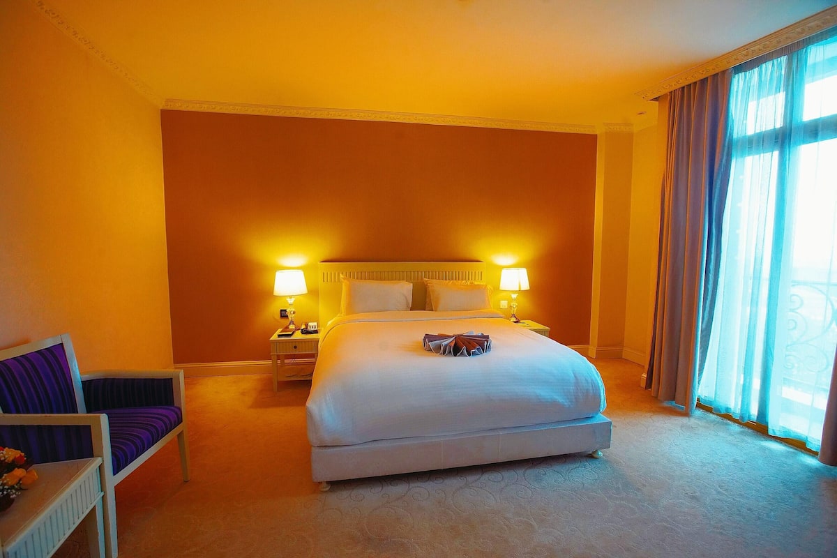 A hotel room with a large bed, two bedside lamps, a chair, and a nightstand.