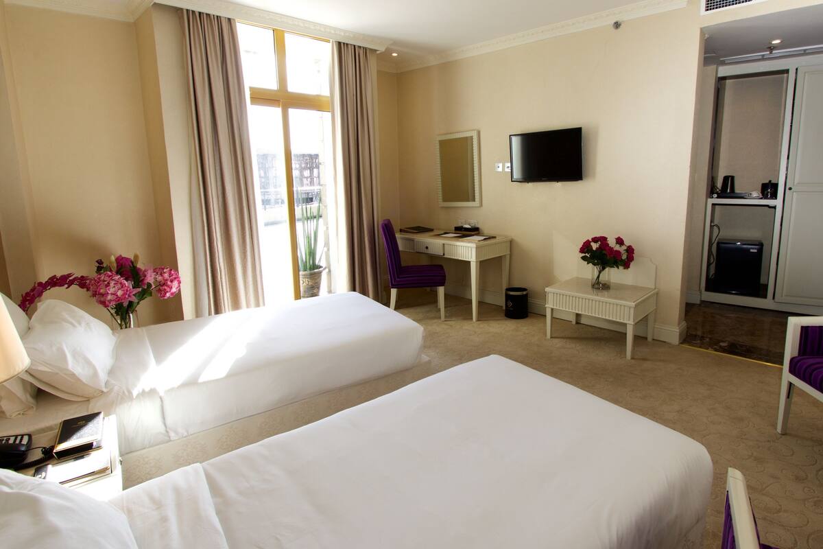 A hotel room with two beds, a desk, a chair, a TV, and a bathroom.