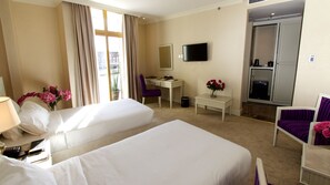 A hotel room with two beds, a desk, a chair, a TV, and a bathroom. - Bellevue Hotel and Spa (Addis Ababa)