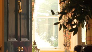 Una habitación con una puerta de madera oscura, una ventana con cortinas florales y una mesa con sillas.