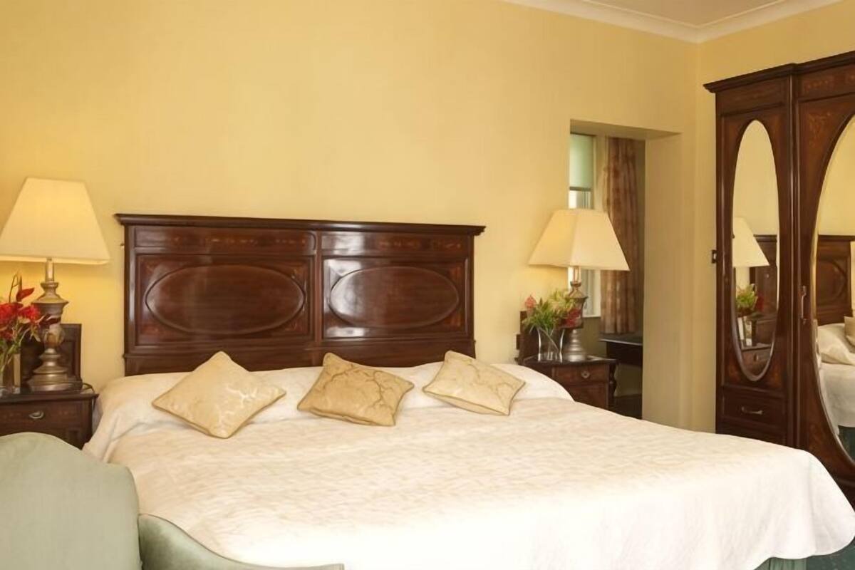 Una habitación de hotel con una cama grande, dos mesitas de noche, un espejo y un sillón verde.