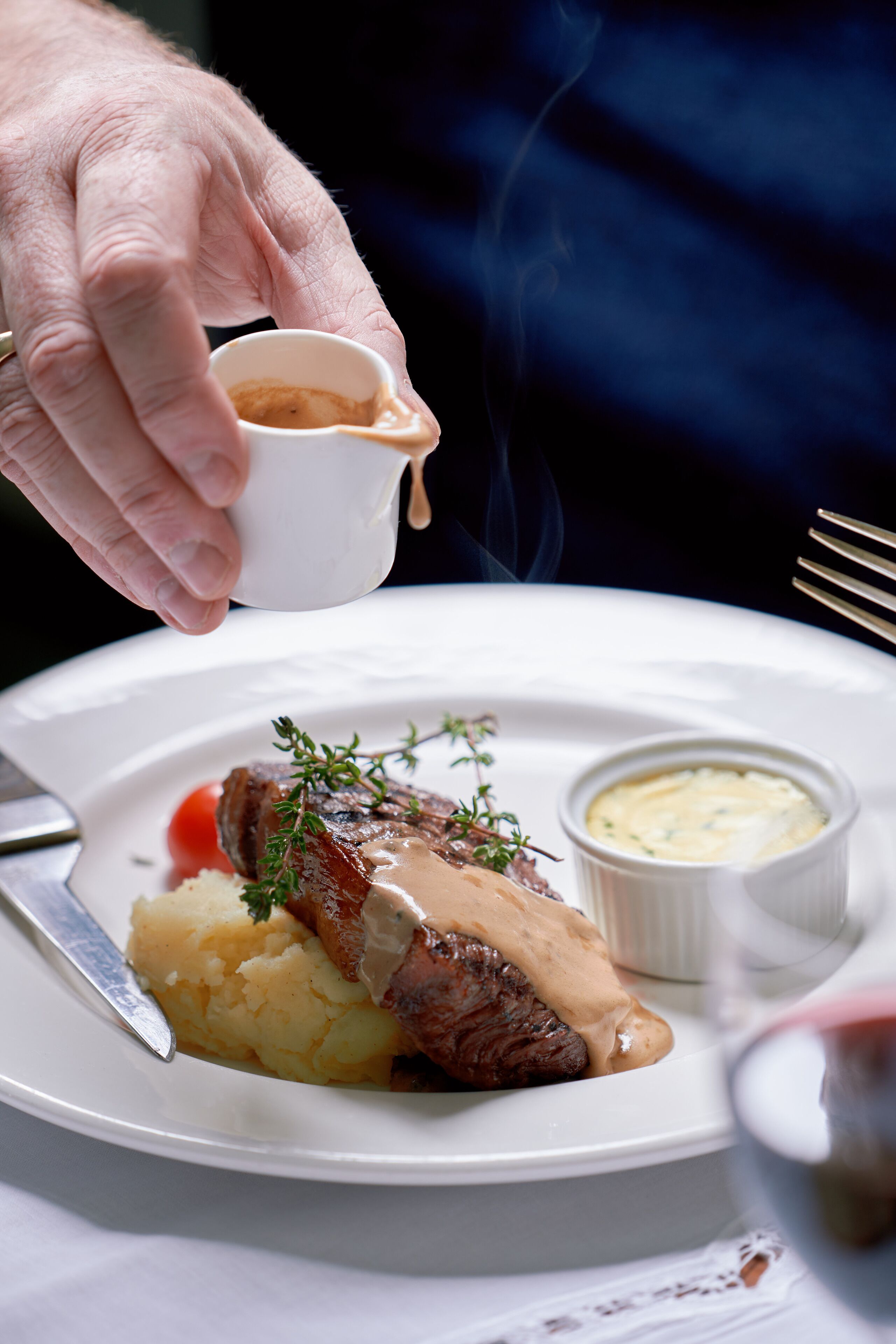 A plate with mashed potatoes, a piece of meat, and a small bowl of sauce.