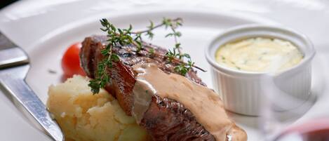 A plate with mashed potatoes, a piece of meat, and a small bowl of sauce.