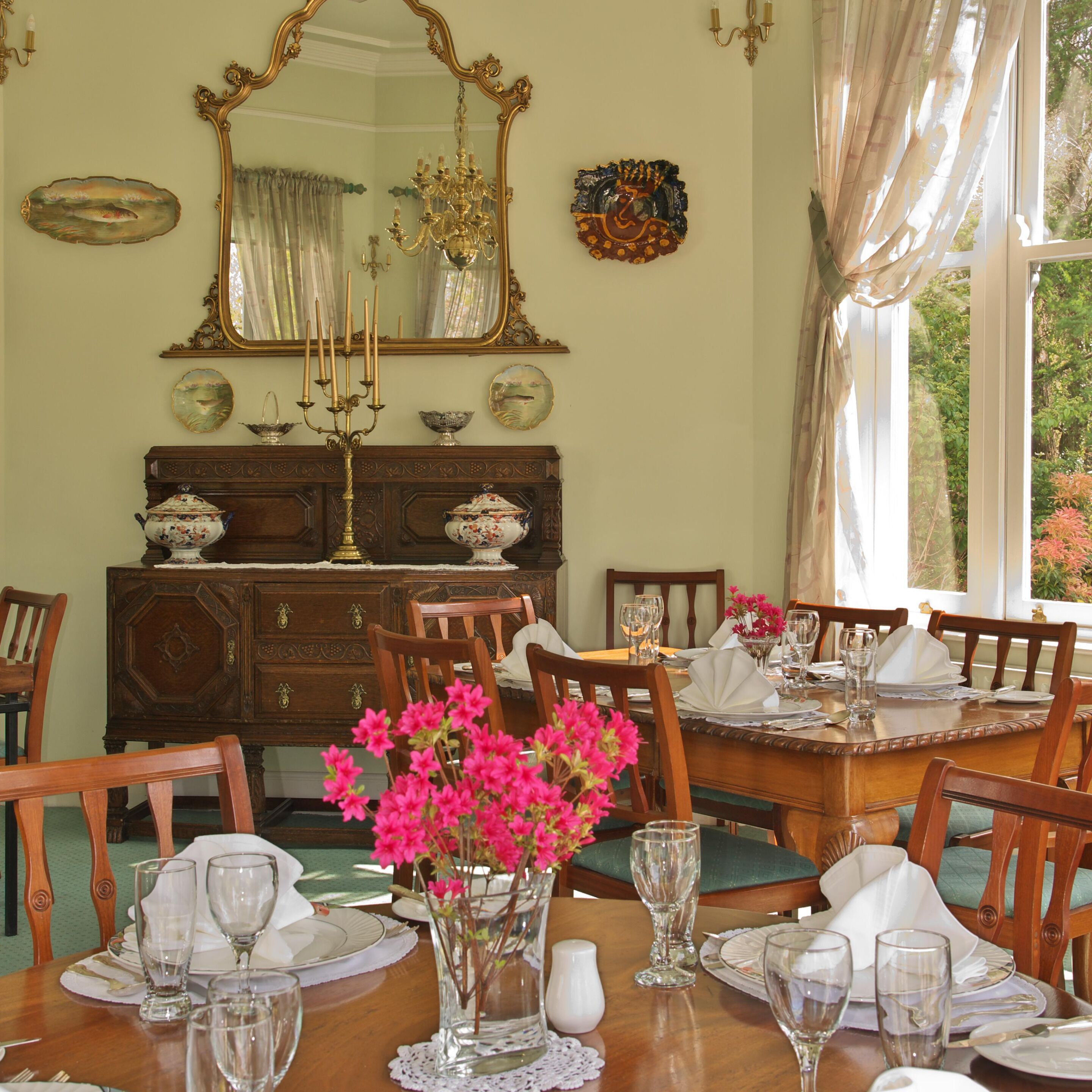 A dining room with a wooden table set for a meal, surrounded by chairs, a large mirror, and a chandelier.