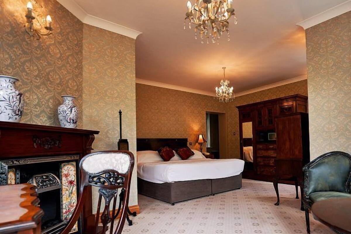 Una habitación de hotel con una cama, una lámpara de araña, un escritorio con una silla y un armario.