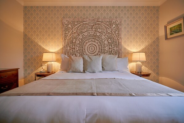 A neatly made bed with white linens and pillows, two bedside lamps, and a decorative tapestry on the wall. - Seaview House Hotel (Bantry)