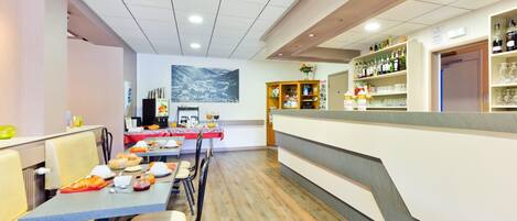 A restaurant with a long counter, multiple tables, and a bar area with shelves of bottles and glasses.