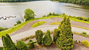 A lake surrounded by lush green hills, a winding road, and a few boats docked near the shore. - Hôtel Restaurant Belle Vue (Les Ancizes-Comps)