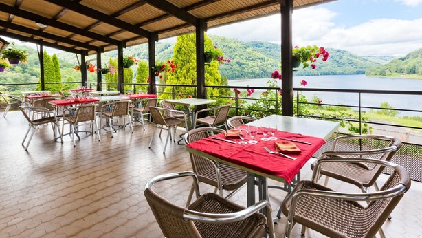 A covered outdoor dining area with tables and chairs, overlooking a lake and hills. - Hôtel Restaurant Belle Vue (Les Ancizes-Comps)