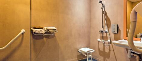 A bathroom with a shower, a sink, a toilet, and a handrail.