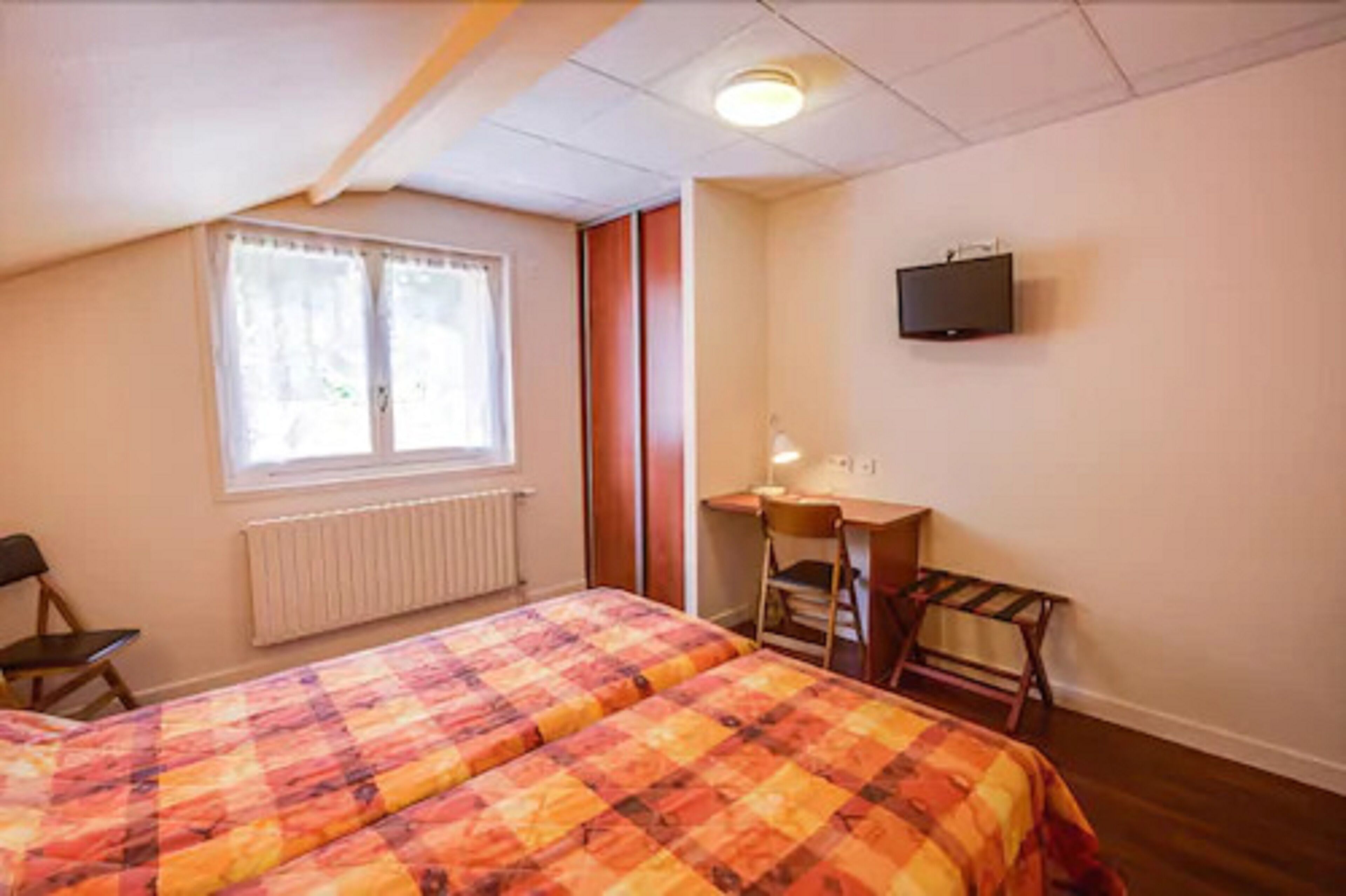 Ein Schlafzimmer mit zwei Betten, einem Schreibtisch, einem Stuhl, einem Heizkörper und einem Fernseher an der Wand.