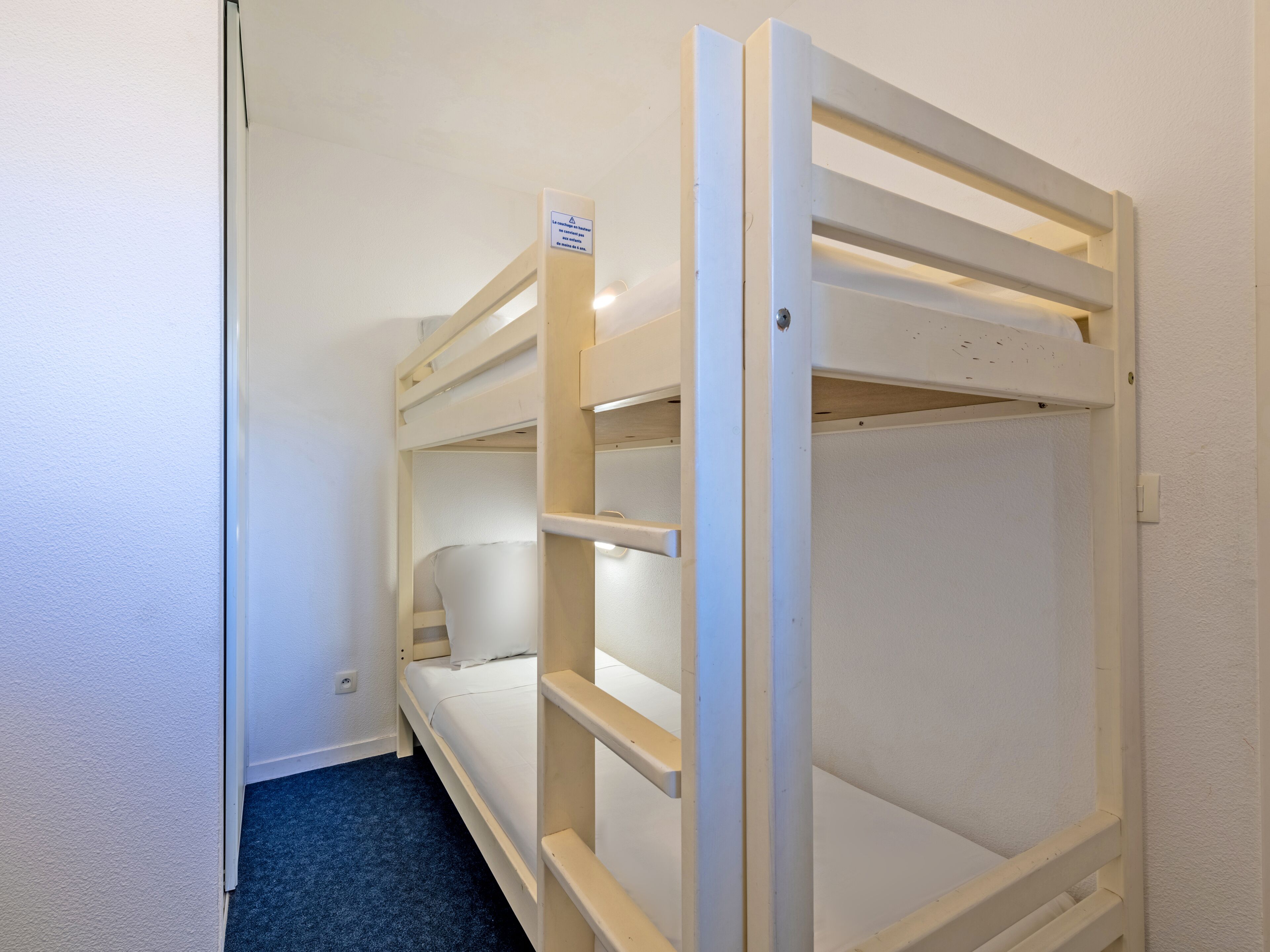 Une chambre avec un lit superposé, un mur blanc et une moquette bleue.