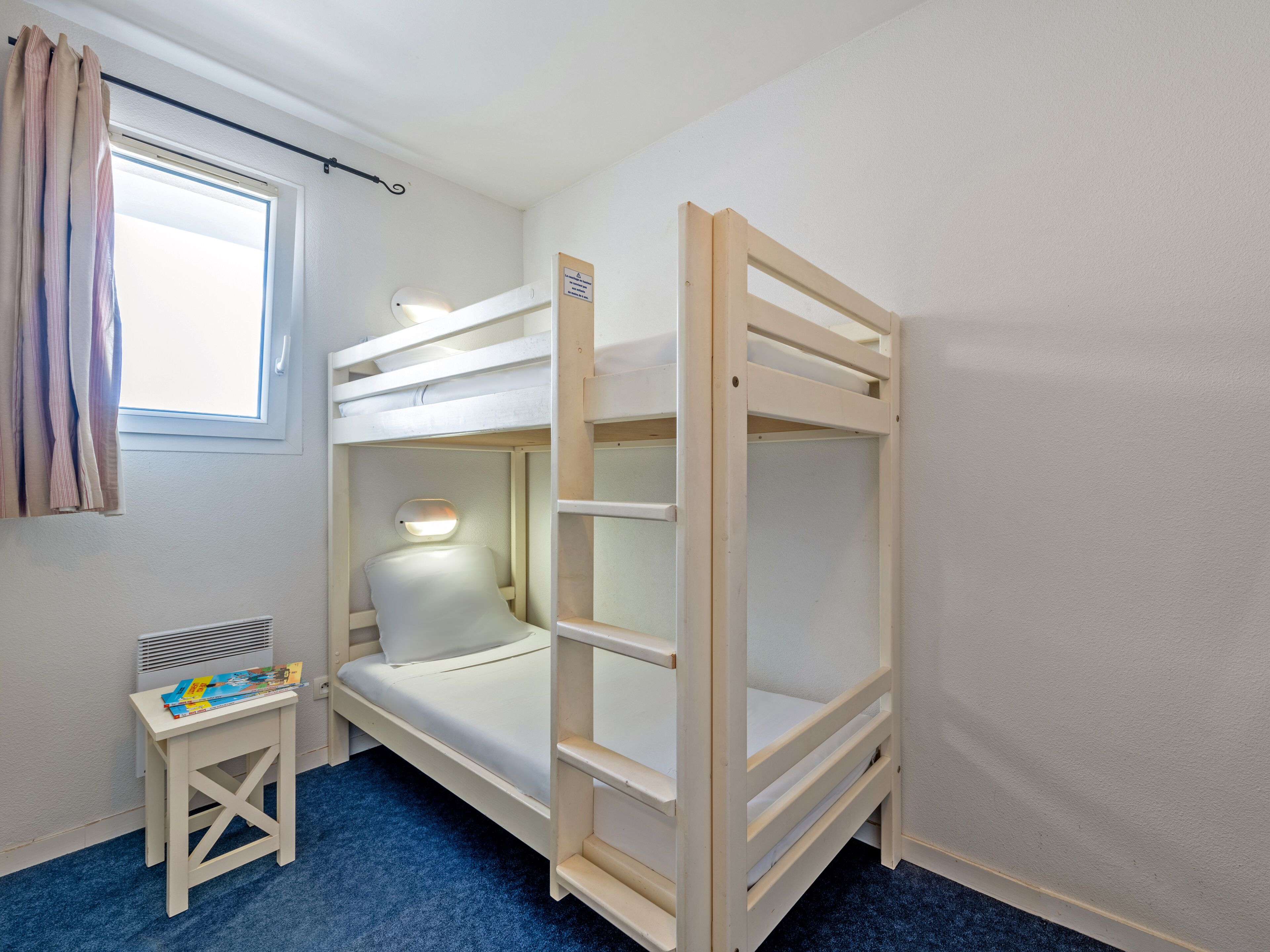 Un lit superposé avec un bureau et une chaise, une fenêtre avec des rideaux et un tapis bleu.